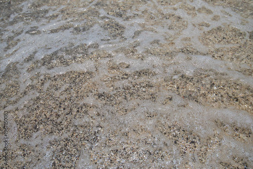 Closeup of beach sand background with small waves and pebbles