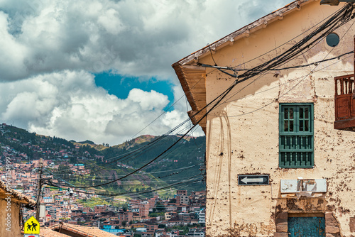 View of a traditional colonial building on a street corner in Cusco, Peru with a densely built hillside neighborhood in the background