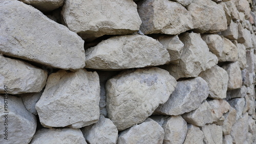 a fragment of a stone wall or fence made of large, rough, solid granite boulders, viewed from an angle in receding perspective, as a textured antique exterior detail