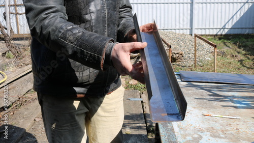 An unrecognizable worker holds a feeder made from bent sheet metal, designed to fit in a cage for small farm birds. Making household iron products yourself.