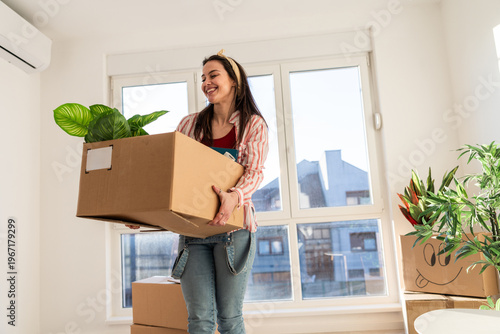 Woman carries a box with a plant while moving into a new apartment during daylight hours
