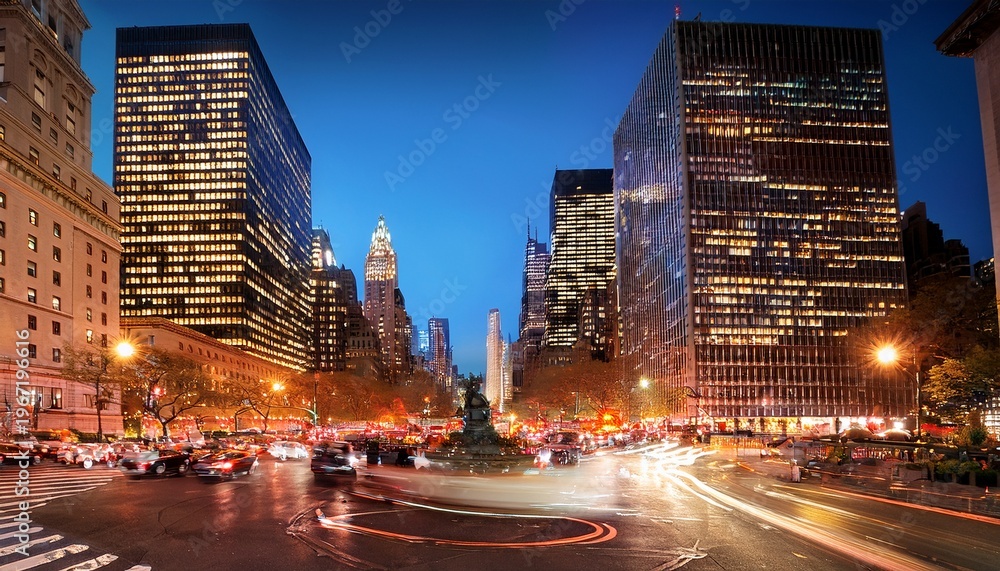 Naklejka premium illuminated cars driving around columbus circle in the bustling new york city at night