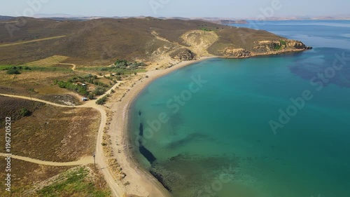 High-angle aerial view of the Neftina Beach on Limnos Island, Greece, showing crystal clear turquoise waters meeting a sandy shoreline backed by rugged, arid Mediterranean hills.