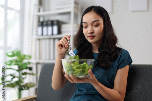 Beautiful healthy Asian woman happily eating delicious vegetable salad at home. Beautiful girl in enjoy eat clean vegetables after exercise for health in house. Diet and Healthy food.