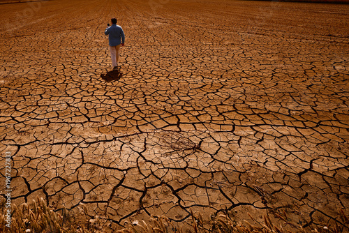 Bild auf Leinwand Man walking across a field of cracked dry soil while using a smartphone