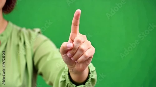A woman's hand pointing upwards in front of a green screen background, possibly for a presentation or virtual interaction