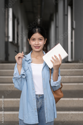 Portrait beautiful Asian woman student. Smile girl happy study. Hold book on the head college campus. young female on international Asia University. Education, study, school, learning, exam.