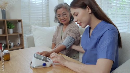 Caregiver elderly home care nurse with senior woman, blood pressure monitor and support, gentle guidance fosters trust and comfort, calm monitoring at wooden table in living room with natural light