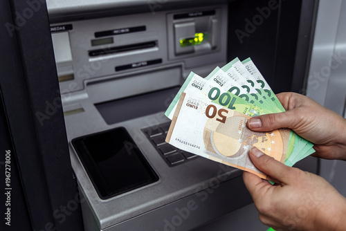 Hands holding various euro banknotes while using an ATM, showcasing cash withdrawal process with modern banking technology and financial transactions