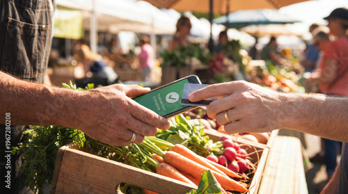 Close up of customer tapping credit card on smartphone held by merchant for contactless payment at sunny outdoor farmers market over wooden crate of fresh carrots and radishes with blurred stalls