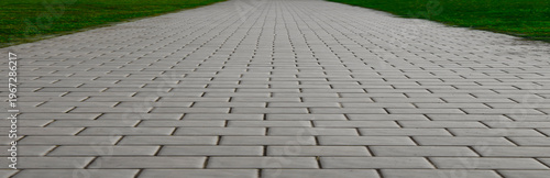 Monotone gray brick stone pavement creates a unique perspective view on the ground, perfect for street roads, sidewalks, and driveways, complemented by green grass.