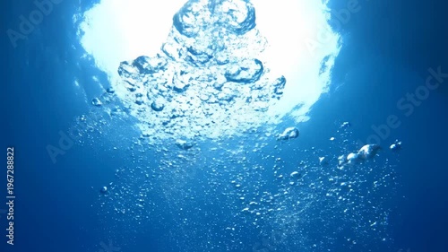 Bubbles rising through clear blue ocean water towards bright sunlight, capturing the beauty of underwater life