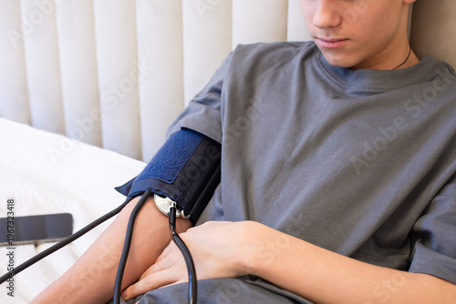 Teenage patient having blood pressure measured with manual sphygmomanometer in bed. Home medical check, pediatric care and hypertension monitoring concept.