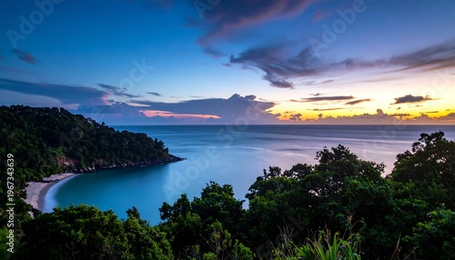 A vibrant sunset bathes a tranquil bay. Lush green foliage frames the view of the beach, ocean, and the colorful sky