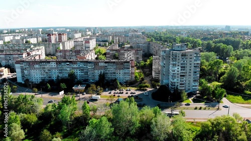 Drone shot of the 10th microdistrict in Sumy, Ukraine, with densely built-up residential buildings in a typical residential area. Busy road with moving traffic, green urban areas. 
