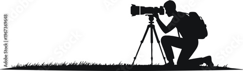 A photographer in a serene outdoor setting, kneeling on the grassy ground to focus his camera on a distant subject. The simplicity of the black silhouette against a white background highlights the ar