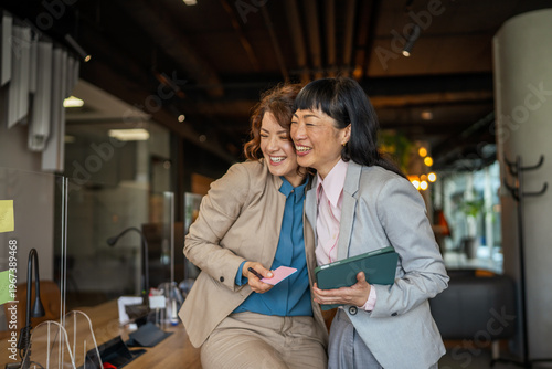 Fotografie Business women laughing together sharing joyful office moment