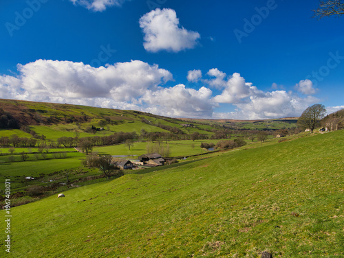 Bright green fields and rolling hills stretch across a valley near Gouthwaite Reservoir toward Middlesmoor in Yorkshire UK under dramatic white clouds