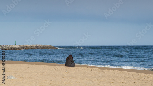 Mujer sola sentada frente al mar en la playa.