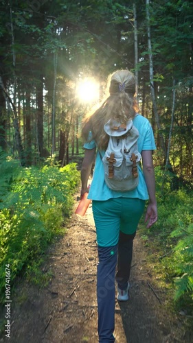 Woman with backpack walking on sunlit forest path in Norway. Authentic lifestyle, mental health wellness and sustainable solo travel concept in Northern Europe.