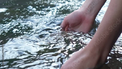 Young woman drinking fresh water from a clean forest stream in summer. Pure nature, peace, and refreshment. A quiet moment in the wilderness, symbol of connection with nature and natural living.