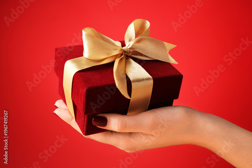 Woman holding beautiful gift box against red background, closeup