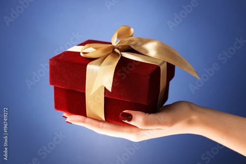 Woman holding beautiful gift box against blue background, closeup