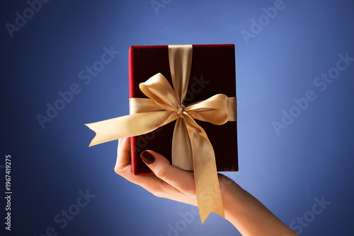 Woman holding beautiful gift box against blue background, closeup