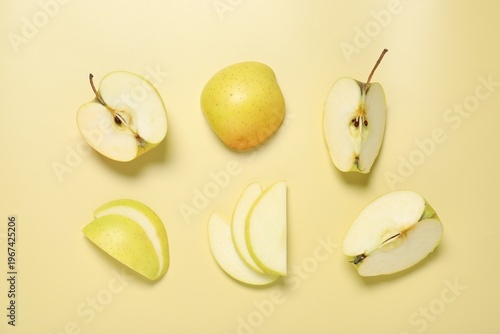 Cut fresh apples on pale yellow background, flat lay