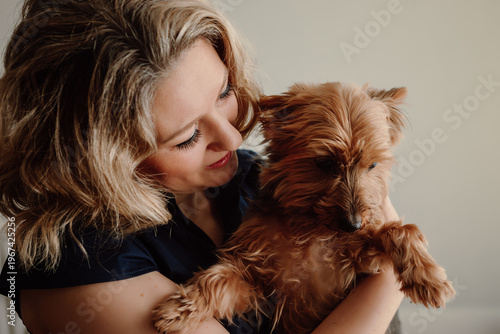 Woman holding small dog looking at pet with affection indoors