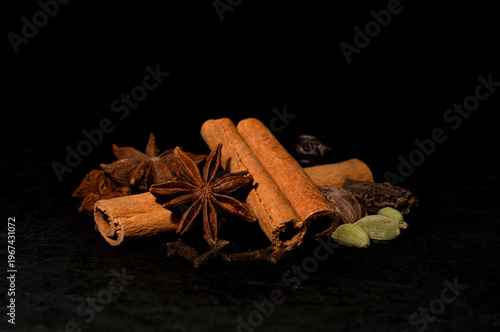 Aromatic whole spices including cinnamon sticks, star anise and cardamom on dark background