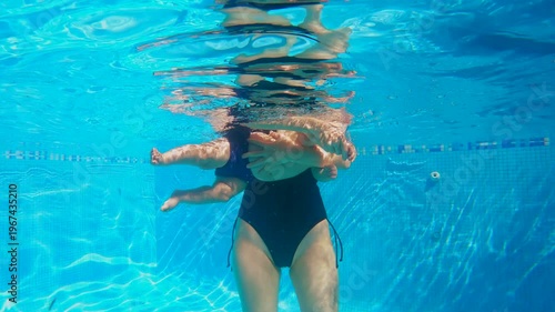 Underwater shot of swim instructor guiding six month old baby boy through infant swimming exercises. Relaxing and stretching routine preparing baby for water skills. Slowmotion video.