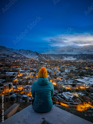 Konstfotografi Person in winter clothes sitting and overlooking the glowing city lights of snow