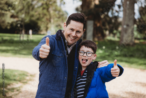 Tableau sur toile Father and son showing thumbs up smiling together outdoors in park
