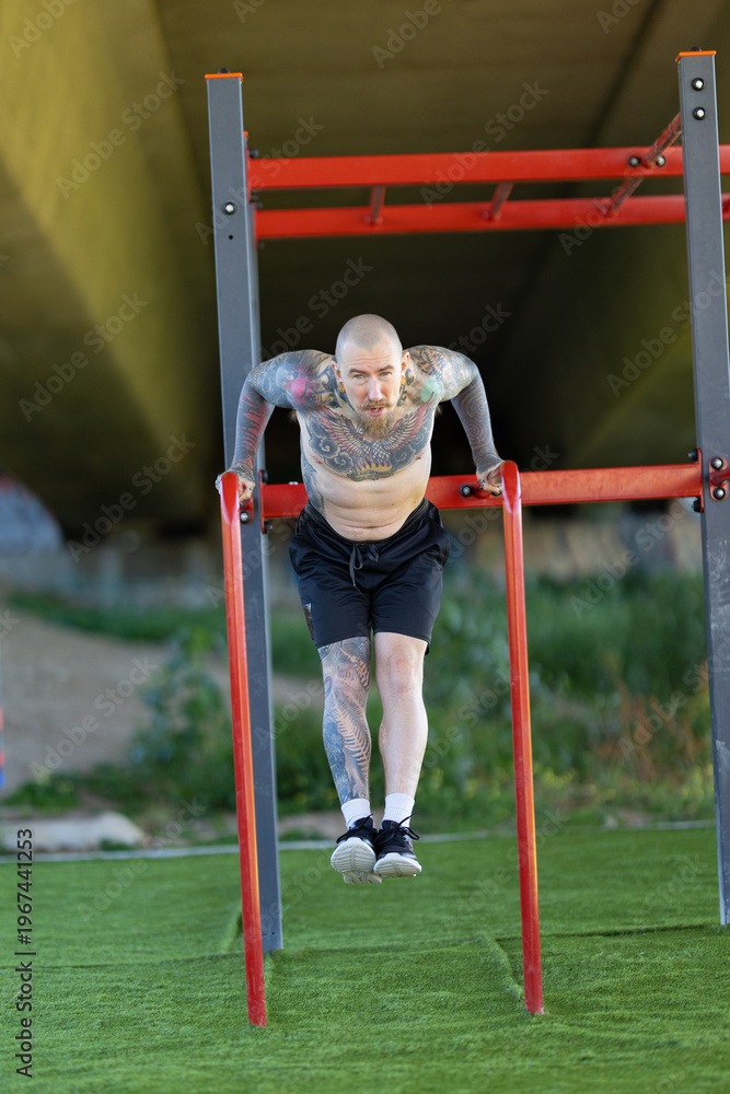 Obraz premium Strong man performing calisthenics dips on parallel bars