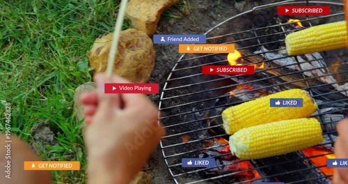 Rotating hands turning skewers and corn over coals at fire pit with hiking shoes, showing alerts