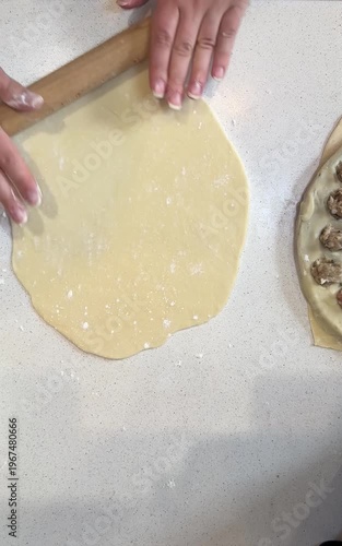 A person's hand pressing rolled dough over a black round dumpling mold on a floured surface during homemade dumpling preparation.