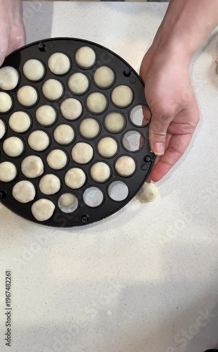 A person's hand pressing rolled dough over a black round dumpling mold on a floured surface during homemade dumpling preparation.