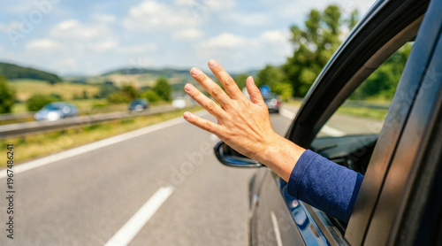 Hand waving from the open window of a moving car on a highway. Close up of an arm reaching out of a vehicle during a road trip