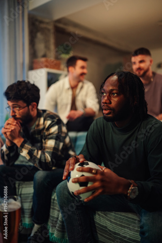 Diverse friends eagerly watching football match at home together, celebrating sport and teamwork