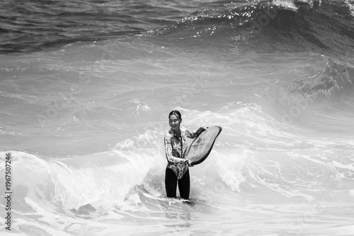 A beautiful girl surfs in a jumpsuit in the middle of the ocean waves