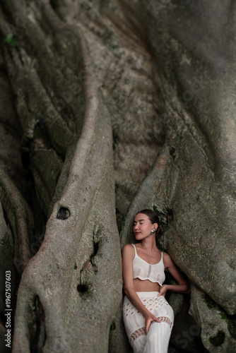 A beautiful girl in an elegant dress poses near an old tree