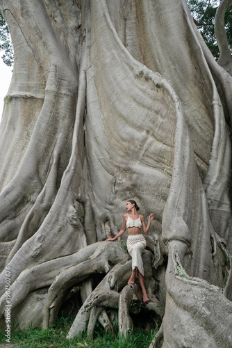 A beautiful girl in an elegant dress poses near an old tree