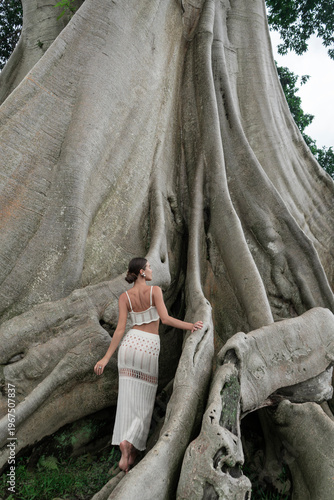 A beautiful girl in an elegant dress poses near an old tree