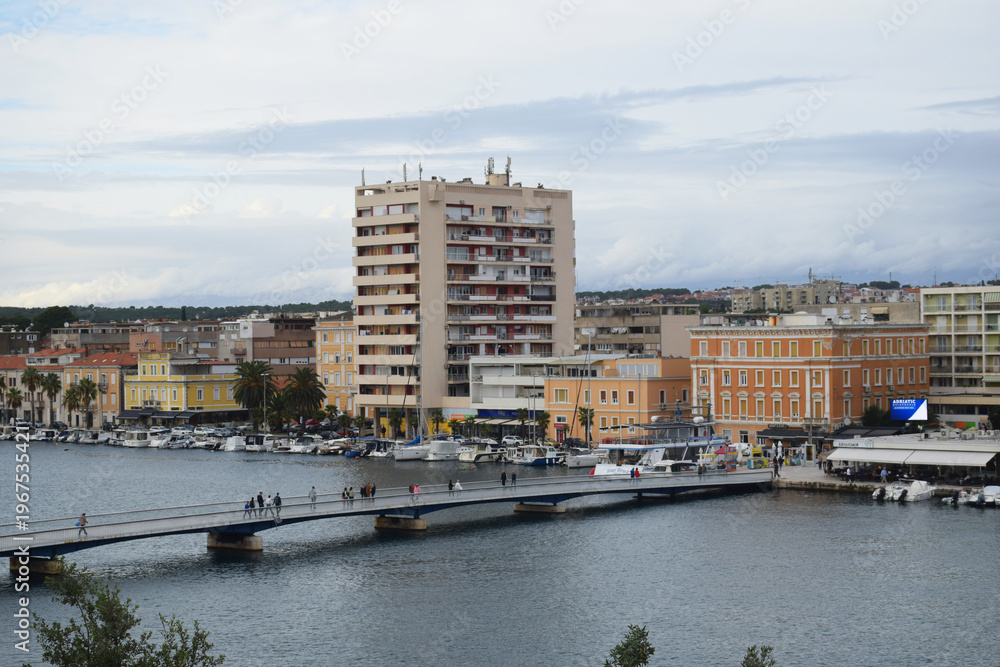 Fototapeta premium Zadar waterfront cityscape in Croatia with marina, bridge, and Adriatic sea view. European coastal town featuring buildings, boats, and calm harbor water reflections. Scenic urban landscape with sea