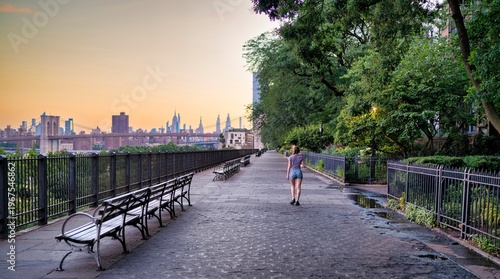 Peaceful riverside walkway with Brooklyn Bridge and Manhattan skyline at sunset in New York City