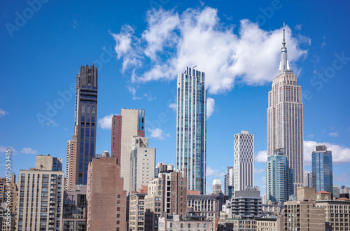 View of New York City skyline showcasing iconic Manhattan landmarks, buildings and skyscrapers on sunny day with clear blue sky.