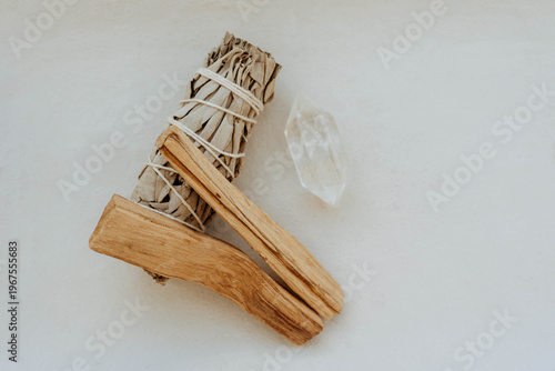 White sage bundle, palo santo stick and clear quartz crystal on light background