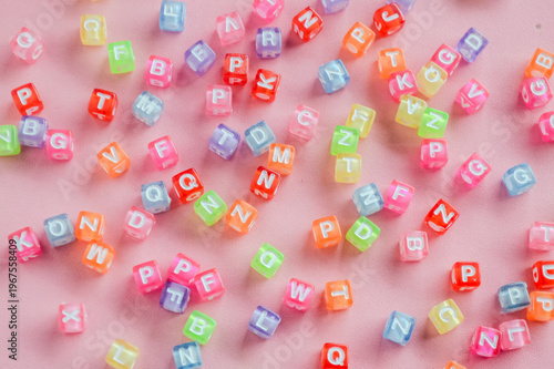 Colorful plastic beads. Top View of Colorful Alphabet Letter Beads Scattered on Pink Background