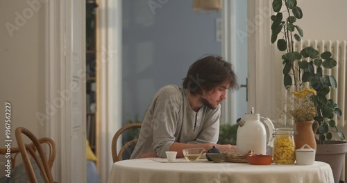 A young man savors his breakfast quietly at a sunny table filled with green plants